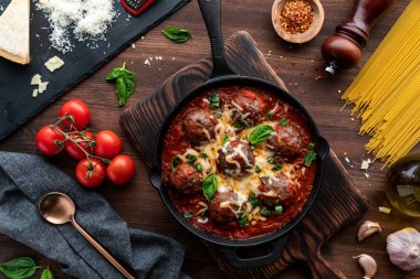 Erimiş peynir ve fesleğenle kaplı soslu köftelerle dolu dökme demir tavanın üst tarafı..