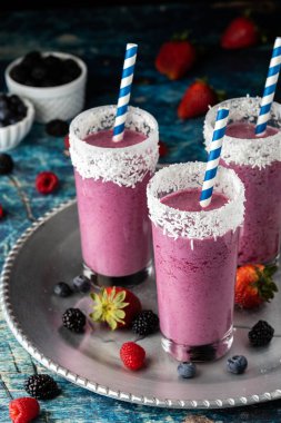 Çeşitli meyvelerle çevrili metal bir tepside mavi çizgili kamışlı meyveli içecekler..