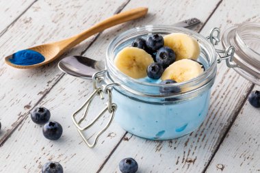 Üzeri yabanmersini ve muz dilimleriyle kaplı mavi spirulina yoğurt parfe..