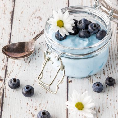 Yaban mersinli bir kavanozda mavi spirulina yoğurdu ve yenilebilir bir papatya, yemeye hazır..