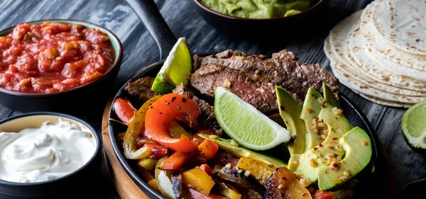 Sos ve tortilla ambalajlarıyla çevrili fajita yapmak için malzemelerle dolu bir tavanın dar görünümü.