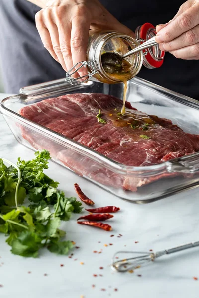 Close-up de um chefe mãos derramando escabeche em um flanco de carne crua. — Fotografia de Stock