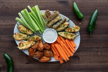 İştah açıcı bir tabak kanat, jalapeno poppers ve havuç ve kereviz çubuklarıyla servis edilen kabak çubukları..