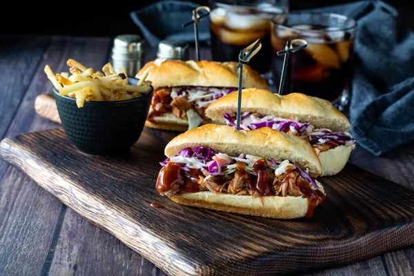 Tres deslizadores de cerdo tirados en una tabla de madera servida con papas fritas y dos bebidas cola por detrás. — Foto de Stock