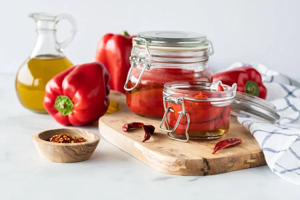 Pieczona czerwona papryka w słoikach otoczona czerwoną papryką, papryką chili i oliwą z oliwek. — Zdjęcie stockowe