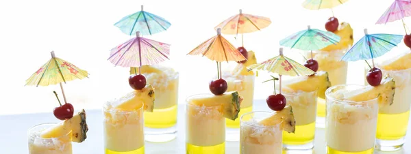 Narrow view of several pineapple jelly parfaits garnished with pineapple, cherries and umbrella picks.