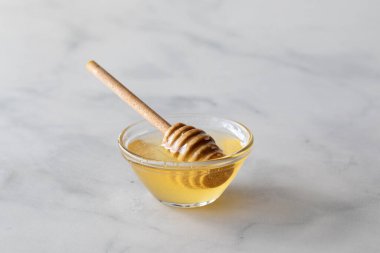 Tahta bir değnekle mermer bir tezgahın üzerinde saf cam bir bal kasesi.