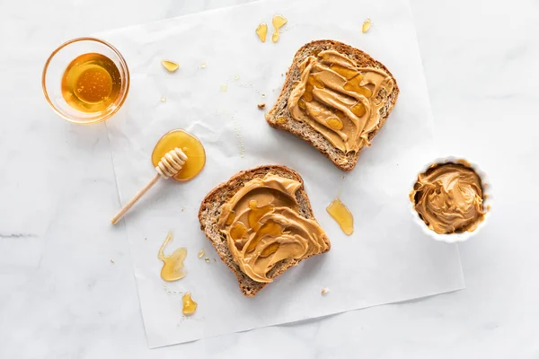 땅콩 버터와 꿀 이 담긴 토스트 두 조각을 맨 위에 펼쳐 놓고 꿀을 사방에 흩어 놓는다. — 스톡 사진