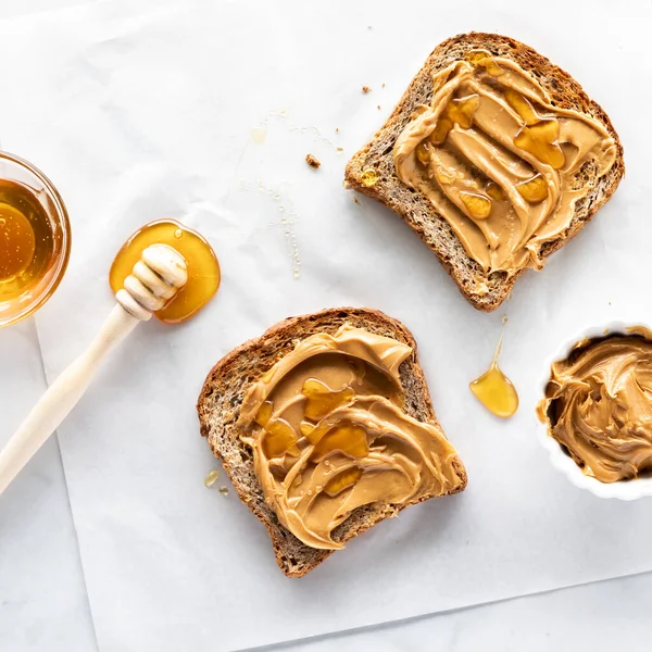 Vista de arriba hacia abajo de dos rebanadas de tostadas multigrano rematadas con mantequilla de maní cremosa y miel. — Foto de Stock