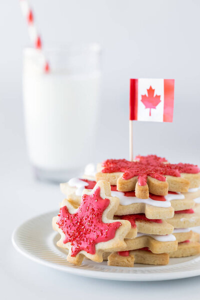 Close up of a stack of Canada flag cookies with a Canada flag at the top and a glass of milk in behind. Stock Image