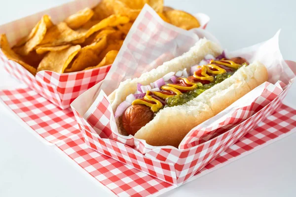 Um cachorro quente coberto com ketchup e mostarda servido com batatas fritas servidas em bandejas quadriculadas de papelão. — Fotografia de Stock