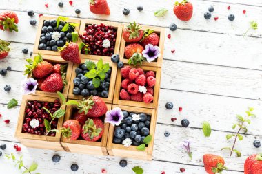 Tahta bir masanın her tarafında çeşitli böğürtlen ve böğürtlen çeşitleriyle dolu ahşap bir kompartıman kutusu..