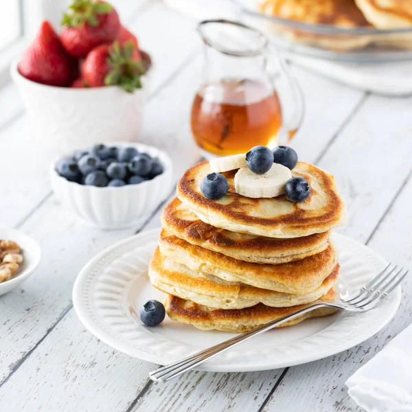 A stack of buttermilk pancakes topped with blueberries and banana, ready for syrup to be poured on top. — Stock Photo, Image