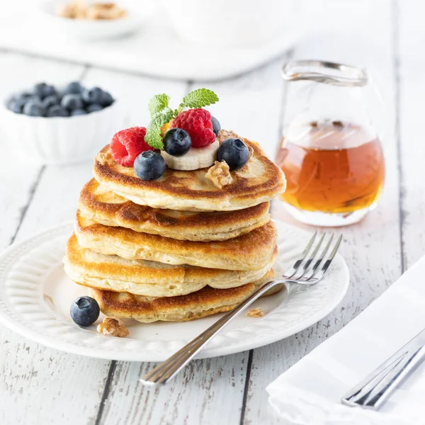 Straight on view of a stack of buttermilk pancakes topped with berries and bananas with syrup in behind. — Stock Photo, Image