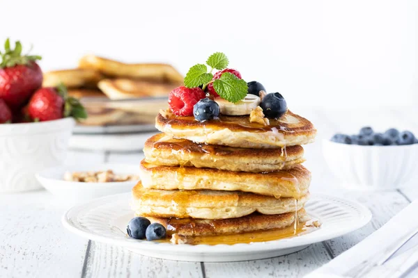 Close up of a stack of buttermilk pancakes topped with berries, banana and syrup and garnished with mint. — Stock Photo, Image