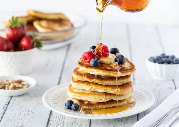 A stack of buttermilk pancakes served with berries and bananas with syrup being poured on top. — Stock Photo, Image