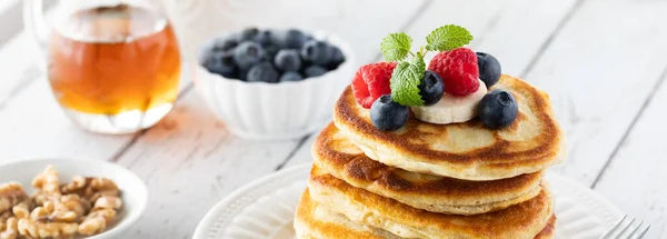 Narrow view of a stack of buttermilk pancakes topped with berries and banana slices and served with syrup and walnuts. — Stock Photo, Image