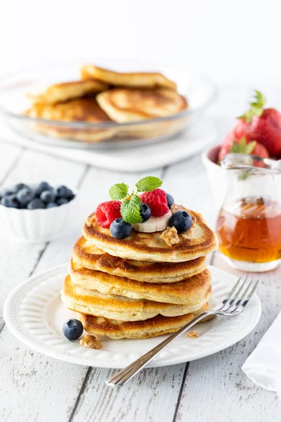 Close up of a stack of buttermilk pancakes, topped with fresh berries and banana slices and served with maple syrup. — Stock Photo, Image