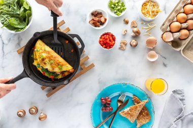 Ellerinin bir spatulayı tuttuğu ve yeni yapılmış bir omleti servis ettiği en tepeden aşağı manzara, onu yapan malzemelerin yanında..