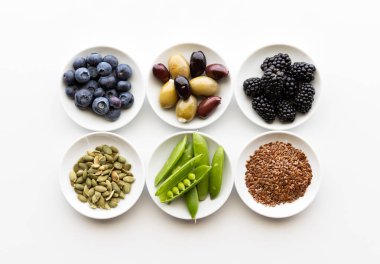 Tohumlar, sebzeler, zeytinler ve böğürtlenler de dahil olmak üzere çeşitli sağlıklı malzemelerden oluşan küçük tabakların yukarıdan aşağı bakışı.