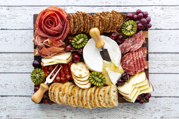 Visão de cima para baixo de uma placa de charcutaria de carne e queijo em uma mesa de madeira leve. — Fotografia de Stock