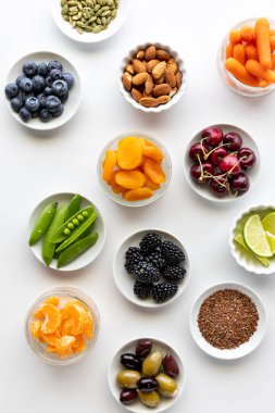 Beyaz arka planda çeşitli sağlıklı organik malzemelerle dolu küçük tabakların yukarıdan görünüşü.