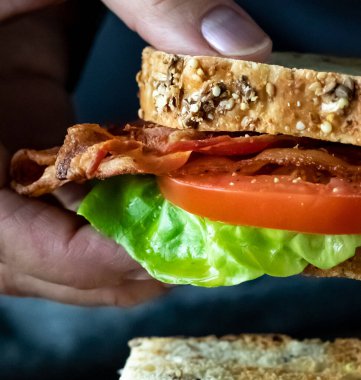 Pastırma ve domatesli sandviç tutan bir elin yakınına..