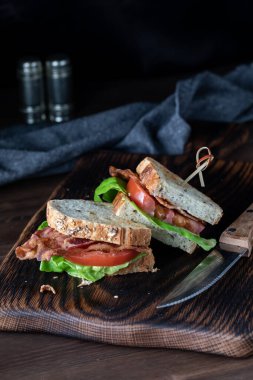 İki parça pastırmalı ve domatesli sandviç, tahta bir tahtanın üzerinde, koyu bir arka planda..