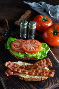 Domatesli, tuzluklu ve biberli ev yapımı domuz pastırmalı ve domatesli sandviçin dikey görüntüsü..