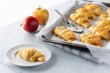 Elma dolgulu hilal rulo küçük bir tabak üzerinde ve arkasında daha fazla pişirme örtüsü, parlak güneşli bir pencereye karşı.