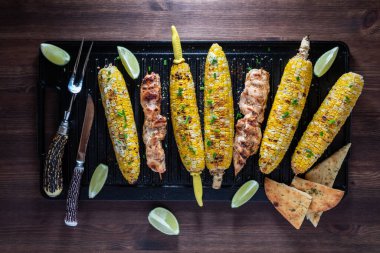 Koçanda ızgara mısır ve dökme demir tavada tavuk şişi..