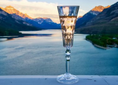 Bir kristal flüt bardağını kapatın. İçi gül şarabı ile dolu. Güzel bir dağ gölü manzarasına karşı..