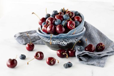 Chelan kiraz ve yaban mersinleriyle dolu çömlek kaseleri parlak bir arka planda duruyor..