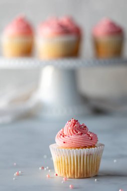 Tek bir vanilyalı kek, pembe kremalı ve serpiştirilmiş ve daha yumuşak bir şekilde arkadaki kaideye odaklı..