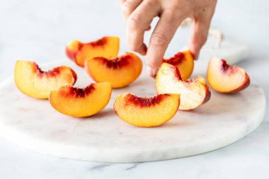 Mermer bir levhadan taze şeftali parçası alan bir el..