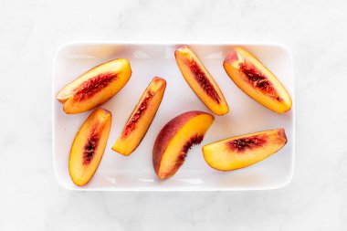 Sulu bir şeftalinin taze dilimlerinden oluşan bir tabağın üstünde..