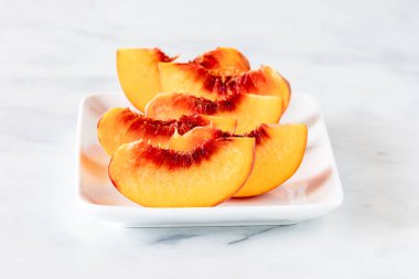 Bedava şeftali şeftali segmentlerinden oluşan beyaz bir tabakta, yemeye hazır..