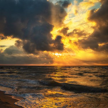 Güneş ışınları desenli bulutların arasından geçiyor. Deniz sahili ve gelen deniz dalgaları hoş bir güneşin doğuşuna ya da batışına karşı. 