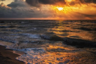 Güneş ışınları desenli bulutların arasından geçiyor. Deniz sahili ve gelen deniz dalgaları hoş bir güneşin doğuşuna ya da batışına karşı. 
