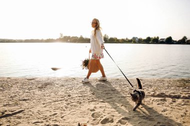 Evcil kediyle sahilde yürüyen kadın.