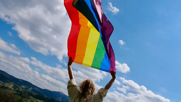 Gökyüzü arka planında LGBT bayrağı tutan kişi