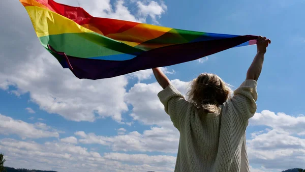 在天空背景下高举LGBT旗的女同性恋 — 图库照片