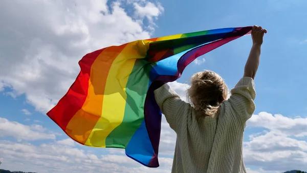 Gökyüzü arka planında LGBT bayrağı tutan kadın — Stok fotoğraf