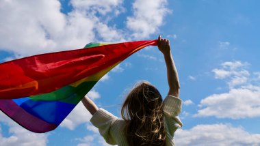 Gökyüzü arka planında LGBT bayrağı tutan lezbiyen