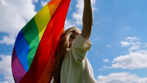 Gökyüzü arka planında LGBT bayrağı tutan kadın