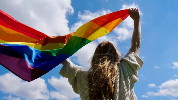 Gökyüzü arka planında LGBT bayrağı tutan kişi