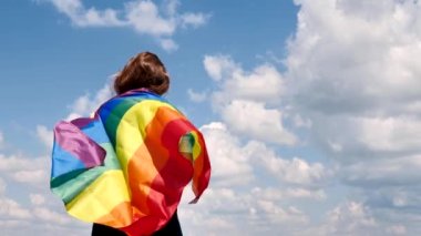 Gökyüzü arka planında LGBT bayrağı tutan kadın