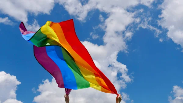 Gökyüzü arka planında LGBT bayrağı tutan kişi — Stok fotoğraf