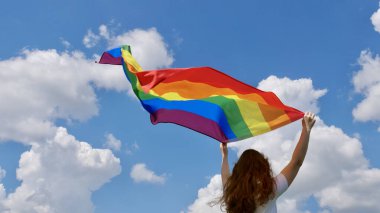 Gökyüzü arka planında LGBT bayrağı tutan kişi
