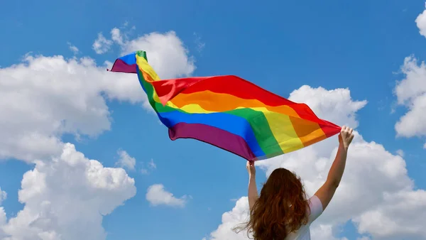 Gökyüzü arka planında LGBT bayrağı tutan kişi — Stok fotoğraf